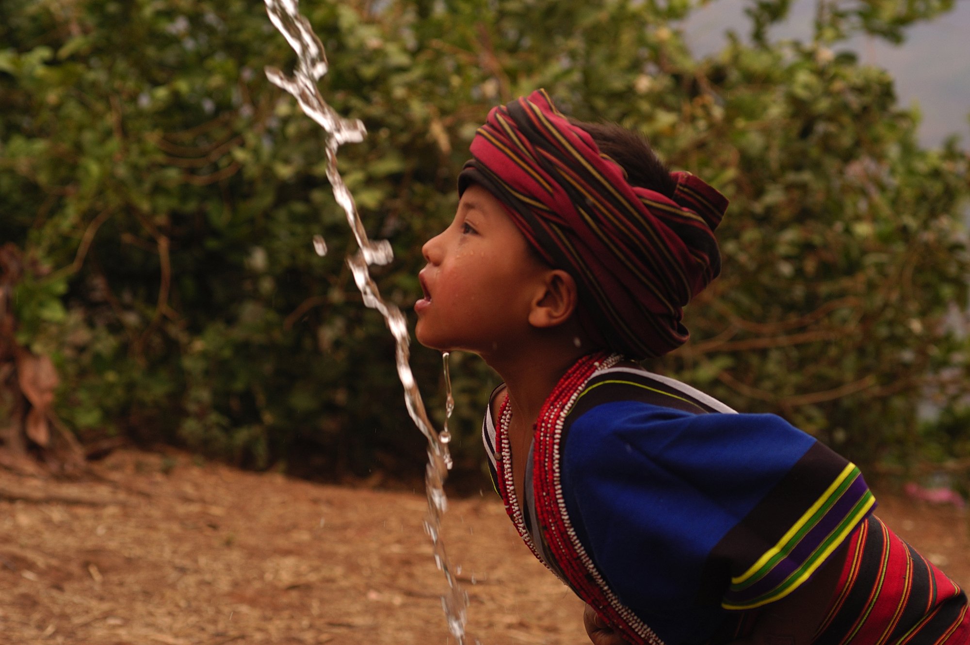 A young chin girl is drinking water under the water tap from gravity flow in Kan Thar Yone village in Southern Chin state in Myanmar